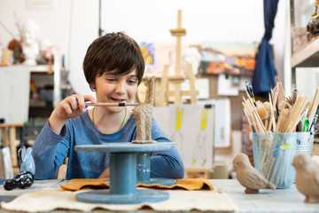Cute handsome boy sculpting clay animal in art school