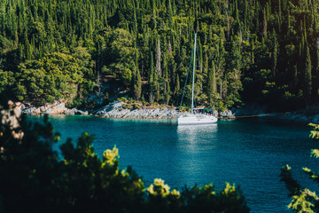 White sail boat yacht moored in the bay of Foki beach with cypress trees in background, Fiskardo,...