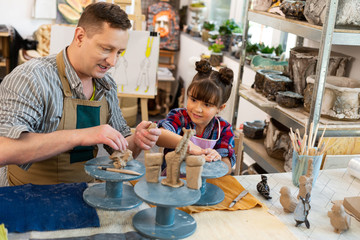 Daughter sculpting clay animals with father working in art school