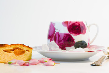  Morning breakfast - a cup of tea with sugar in a mug with pink flowers and a slice of appetizing cheese casserole with raisins on a white background