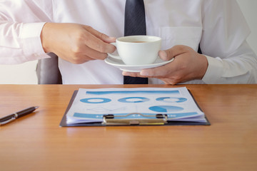 Fototapeta na wymiar Businessman sitting at office desk having a coffee break, he is holding a mug and a digital tablet