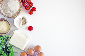Ingredients for pizza, tomatoes, cheese, flour, eggs, yeast on a white background, flat lay, copy space