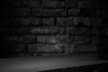 Old wood table with blurred concrete block wall in dark room background.
