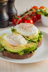 Avocado toast, cherry tomato and poached eggs on wooden background. Breakfast with vegetarian food, healthy diet concept.