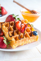 Fresh homemade food of berry Belgian waffles with honey, chocolate, strawberry, blueberry, maple syrup and cream. Healthy dessert breakfast concept with juice