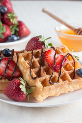 Fresh homemade food of berry Belgian waffles with honey, chocolate, strawberry, blueberry, maple syrup and cream. Healthy dessert breakfast concept with juice