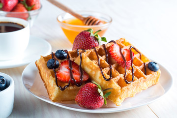 Fresh homemade food of berry Belgian waffles with honey, chocolate, strawberry, blueberry, maple syrup and cream. Healthy dessert breakfast concept with juice