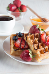 Fresh homemade food of berry Belgian waffles with honey, chocolate, strawberry, blueberry, maple syrup and cream. Healthy dessert breakfast concept with juice