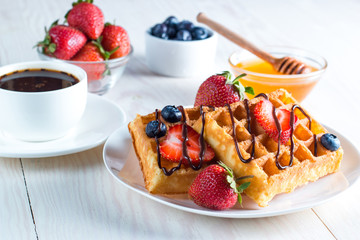 Fresh homemade food of berry Belgian waffles with honey, chocolate, strawberry, blueberry, maple syrup and cream. Healthy dessert breakfast concept with juice