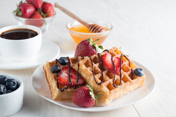 Fresh homemade food of berry Belgian waffles with honey, chocolate, strawberry, blueberry, maple syrup and cream. Healthy dessert breakfast concept with juice