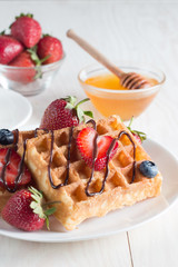 Fresh homemade food of berry Belgian waffles with honey, chocolate, strawberry, blueberry, maple syrup and cream. Healthy dessert breakfast concept with juice