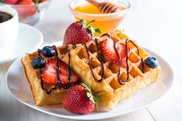 Fresh homemade food of berry Belgian waffles with honey, chocolate, strawberry, blueberry, maple syrup and cream. Healthy dessert breakfast concept with juice