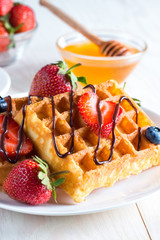Fresh homemade food of berry Belgian waffles with honey, chocolate, strawberry, blueberry, maple syrup and cream. Healthy dessert breakfast concept with juice