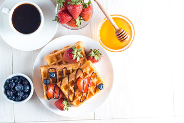 Fresh homemade food of berry Belgian waffles with honey, chocolate, strawberry, blueberry, maple syrup and cream. Healthy dessert breakfast concept with juice
