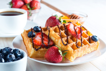 Fresh homemade food of berry Belgian waffles with honey, chocolate, strawberry, blueberry, maple syrup and cream. Healthy dessert breakfast concept with juice