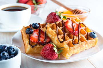 Fresh homemade food of berry Belgian waffles with honey, chocolate, strawberry, blueberry, maple syrup and cream. Healthy dessert breakfast concept with juice