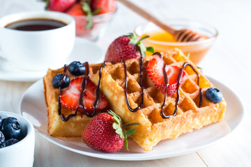 Fresh homemade food of berry Belgian waffles with honey, chocolate, strawberry, blueberry, maple syrup and cream. Healthy dessert breakfast concept with juice
