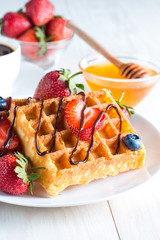 Fresh homemade food of berry Belgian waffles with honey, chocolate, strawberry, blueberry, maple syrup and cream. Healthy dessert breakfast concept with juice