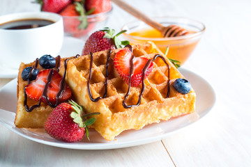 Fresh homemade food of berry Belgian waffles with honey, chocolate, strawberry, blueberry, maple syrup and cream. Healthy dessert breakfast concept with juice