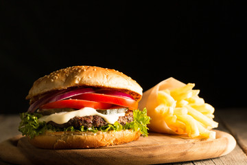 Home made hamburger with beef, onion, tomato, lettuce and cheese. Fresh burger close up on wooden rustic table with potato fries, beer and chips. Cheeseburger.
