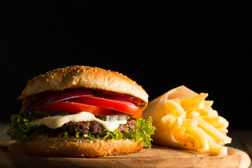 Home made hamburger with beef, onion, tomato, lettuce and cheese. Fresh burger close up on wooden rustic table with potato fries, beer and chips. Cheeseburger.