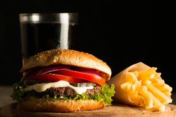 Home made hamburger with beef, onion, tomato, lettuce and cheese. Fresh burger close up on wooden rustic table with potato fries, beer and chips. Cheeseburger.