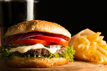 Home made hamburger with beef, onion, tomato, lettuce and cheese. Fresh burger close up on wooden rustic table with potato fries, beer and chips. Cheeseburger.
