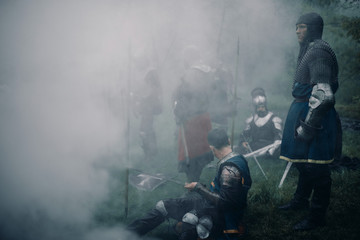 Battle squad of medieval knights of the Crusaders rest in a misty forest.