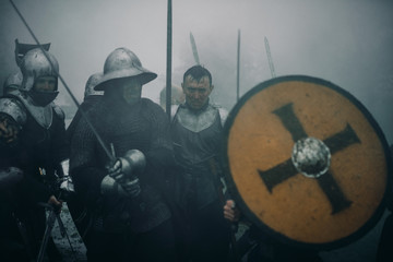 Combat squad of medieval knights of the Crusaders stand in armors preparing to attack in misty...