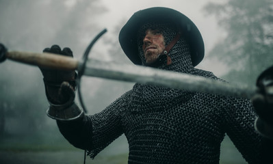 Portrait of medieval knight with his sword in the misty forest.