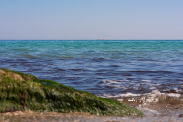 View of the Black Sea on a clear sunny day. On the shore, stones and sand, ships on the horizon. Blue sky and beautiful clouds.