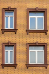 Fototapeta na wymiar 4 plastic windows in the brick house of yellow bricks. Beautiful windows with moldings and brown trim. Modern design of windows, construction of residential buildings