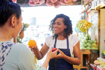 Smiling pretty female fruit vendor helping customer with choosing best fruits