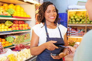 Smiling pretty young grocery store worker with card reader talking to customer