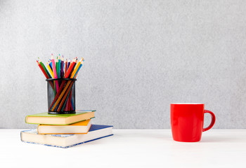 colorful pencils, books and red cup on a desk with gray background