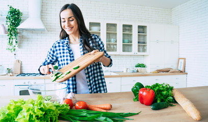 Beautiful young woman is preparing vegetable salad in the kitchen. Healthy Food. Vegan Salad. Diet. Dieting Concept. Healthy Lifestyle. Cooking At Home. Prepare Food. Cutting ingredients on table