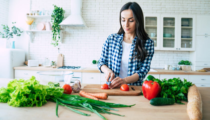 Beautiful young woman is preparing vegetable salad in the kitchen. Healthy Food. Vegan Salad. Diet. Dieting Concept. Healthy Lifestyle. Cooking At Home. Prepare Food. Cutting ingredients on table