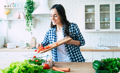 Beautiful young woman is preparing vegetable salad in the kitchen. Healthy Food. Vegan Salad. Diet. Dieting Concept. Healthy Lifestyle. Cooking At Home. Prepare Food. Cutting ingredients on table