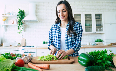 Beautiful young woman is preparing vegetable salad in the kitchen. Healthy Food. Vegan Salad. Diet....