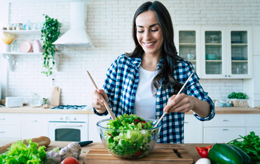 Beautiful young woman is preparing vegetable salad in the kitchen. Healthy Food. Vegan Salad. Diet....