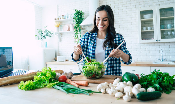 Beautiful young woman is preparing vegetable salad in the kitchen. Healthy Food. Vegan Salad. Diet. Dieting Concept. Healthy Lifestyle. Cooking At Home. Prepare Food. Cutting ingredients on table