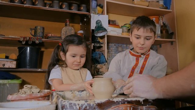 Pottery class and workshop: professional male potter working with children and showing how to make ceramic wares in pottery studio. Handmade, education and study concept