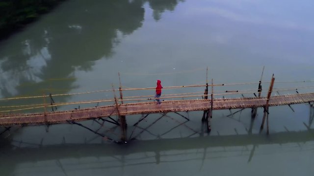 young Girl tourist walks on the bridge of bamboo across the Nam Kahn River in city Luang Prabang. Laos. 4K move drone