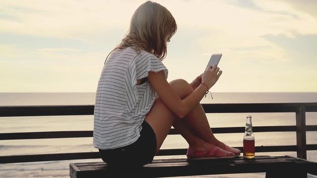 Girl using cellphone on the ocean shore.