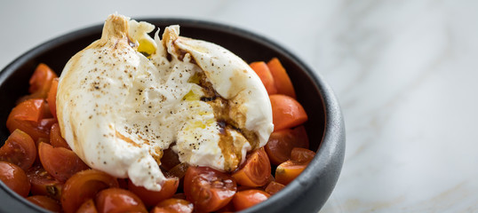 Burrata Büffelmozzarella Kugel mit Tomaten, Olivenöl und Balsamico auf schwarzen Teller