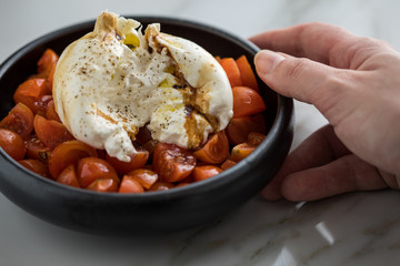 Frau isst Burrata Büffelmozzarella Kugel mit Tomaten, Olivenöl und Balsamico auf schwarzen Teller