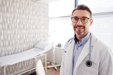 Portrait Of Smiling Mature Male Doctor Wearing White Coat With Stethoscope Standing In Office