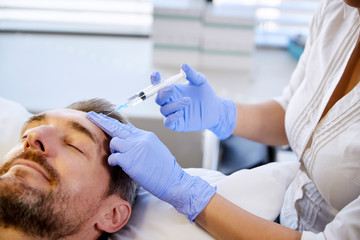 Fototapeta premium Female Beautician Giving Mature Male Patient Botox Injection In Forehead