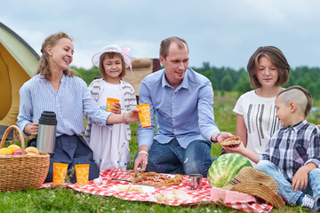 Happy family having picnic in meadow on a sunny day. Family Enjoying Camping Holiday In Countryside