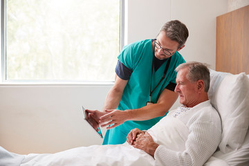 Obraz premium Surgeon With Digital Tablet Visiting Senior Male Patient In Hospital Bed In Geriatric Unit